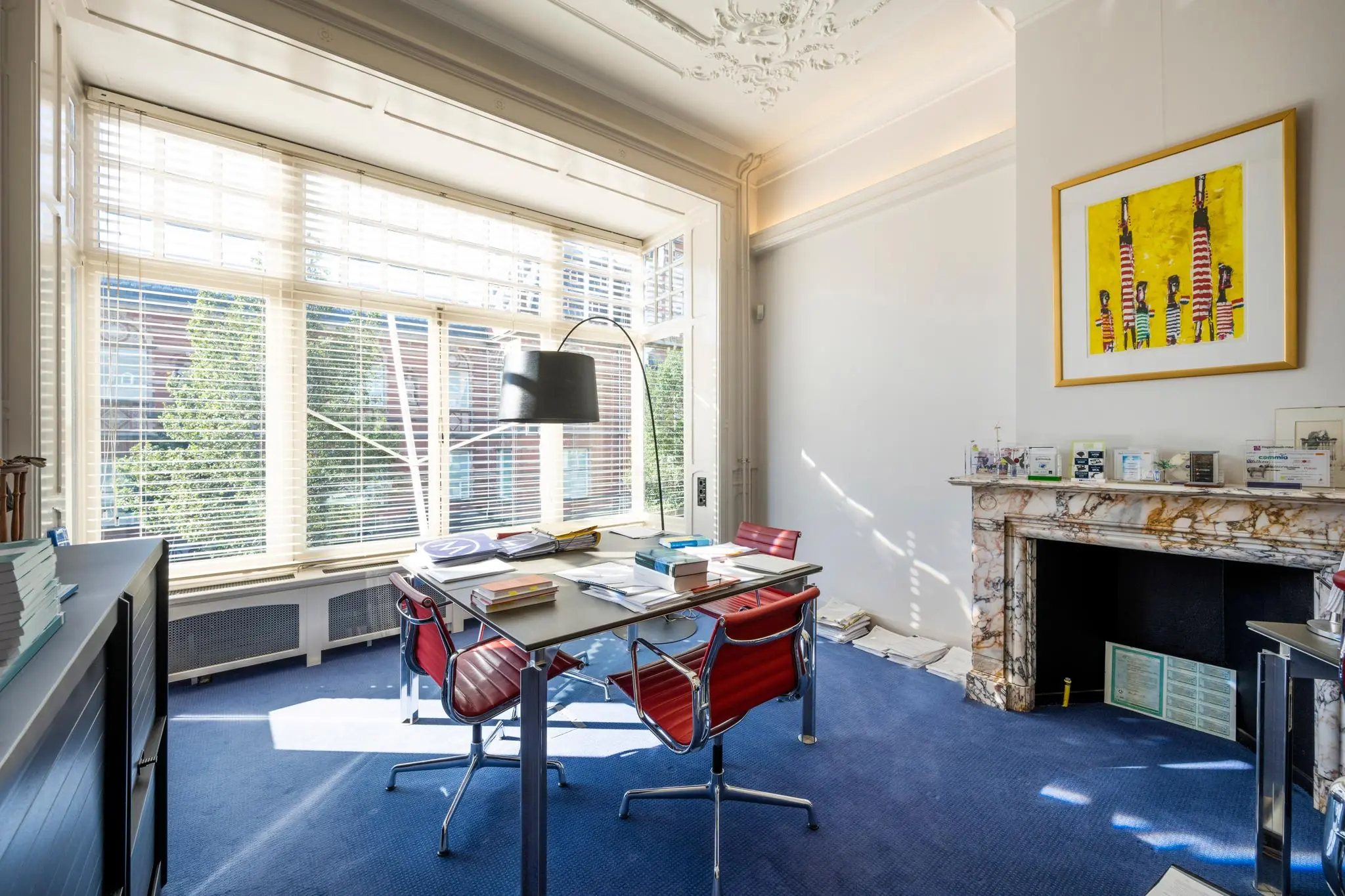 Licht kantoor met grote ramen, een marmeren schouw en een moderne vergadertafel met rode stoelen aan de Paulus Potterstraat.